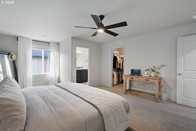 carpeted bedroom with a walk in closet, ensuite bath, ceiling fan, a textured ceiling, and a closet