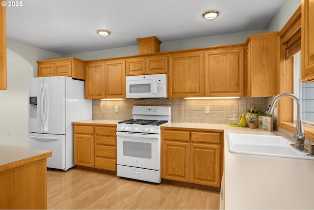 kitchen featuring sink, white appliances, light hardwood / wood-style floors, and backsplash