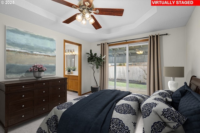 carpeted bedroom featuring connected bathroom, access to outside, ceiling fan, and a tray ceiling