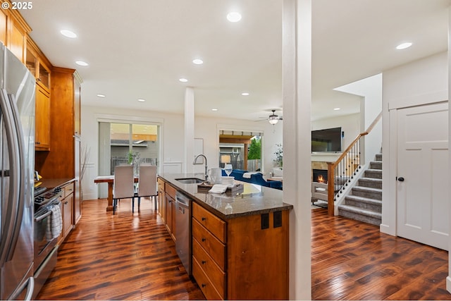 19144 Gentry Highlands Ln, Oregon City, OR 97045 - kitchen featuring a warm lit fireplace, a sink, stainless steel appliances, brown cabinetry, and dark wood-type flooring