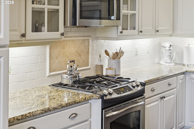 10135 SW Morrison St, Portland, OR 97225 - kitchen with appliances with stainless steel finishes, tasteful backsplash, white cabinets, and glass insert cabinets