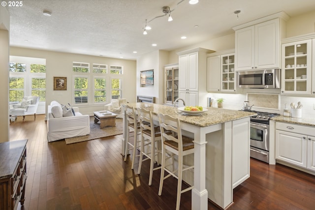 10135 SW Morrison St, Portland, OR 97225 - kitchen with stainless steel appliances, open floor plan, light stone counters, dark wood-style floors, and a kitchen island with sink