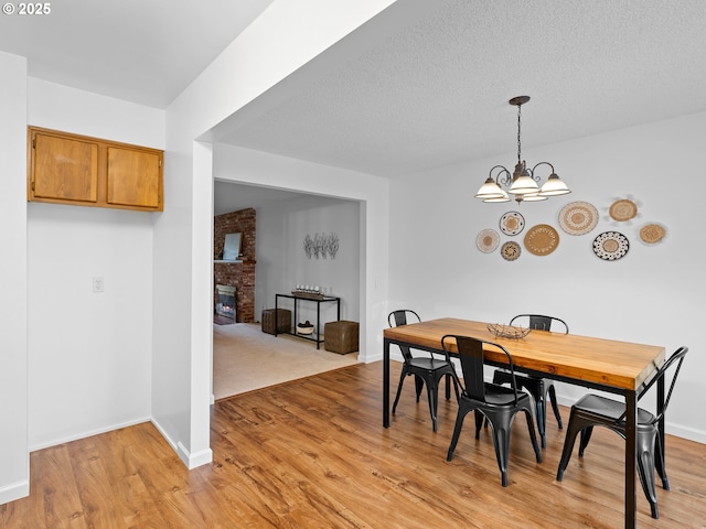 dining space featuring a textured ceiling, light hardwood / wood-style flooring, an inviting chandelier, and a fireplace