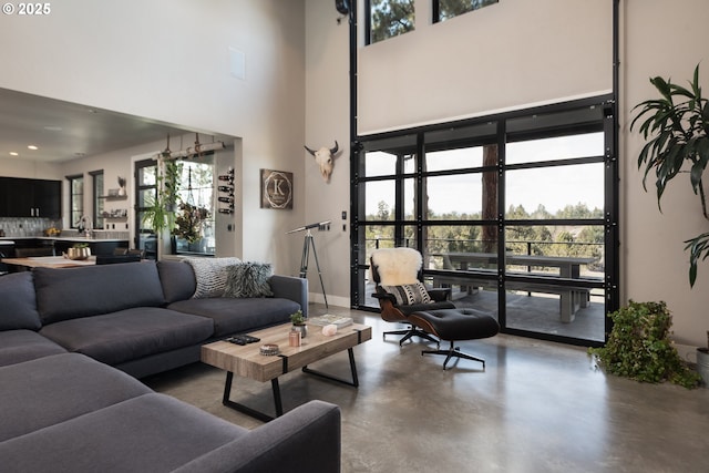 living room featuring finished concrete flooring, a high ceiling, baseboards, and recessed lighting