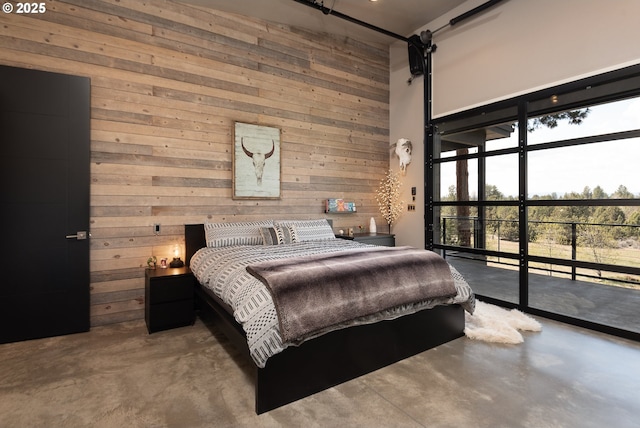 bedroom featuring finished concrete flooring, wooden walls, a towering ceiling, and access to outside