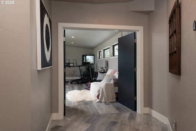 corridor featuring wood finished floors, baseboards, and vaulted ceiling