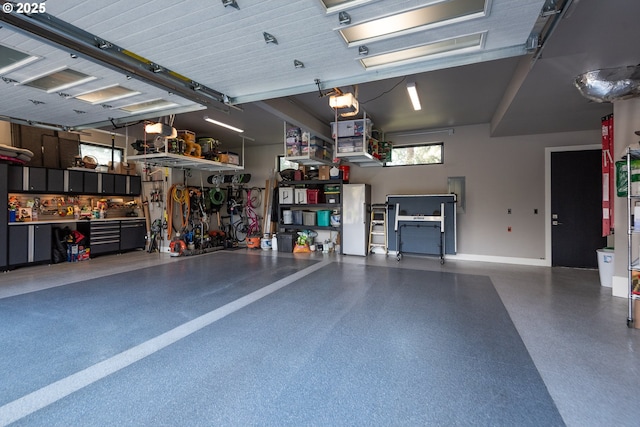garage featuring freestanding refrigerator, baseboards, electric panel, and a workshop area