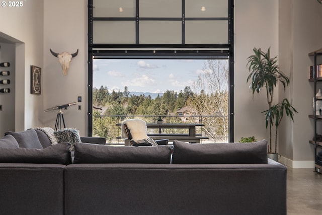 living room featuring concrete flooring, a towering ceiling, and baseboards