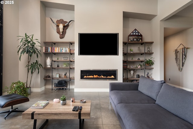 living area featuring concrete floors, a glass covered fireplace, and baseboards