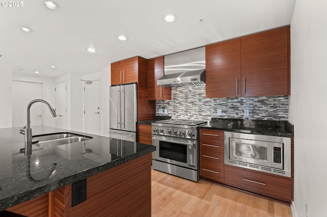 kitchen with premium appliances, tasteful backsplash, a sink, wall chimney range hood, and dark stone countertops