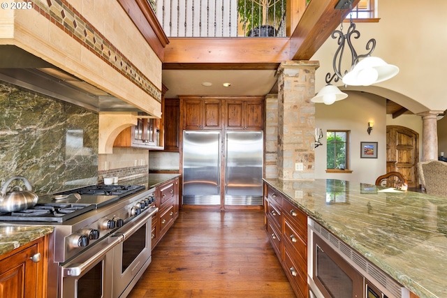 16465 Suntree Ln, Sisters, OR 97759 - kitchen featuring built in appliances, ornate columns, custom range hood, decorative backsplash, and brown cabinets