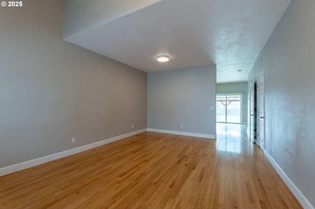 spare room with baseboards, light wood-type flooring, and a textured ceiling