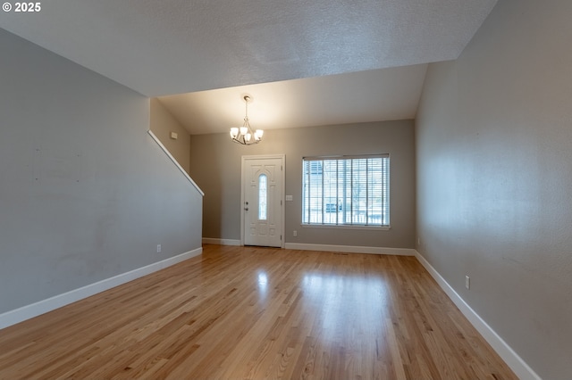 entryway featuring baseboards, an inviting chandelier, light wood-style flooring, vaulted ceiling, and a textured ceiling