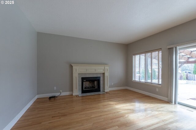 unfurnished living room with a tiled fireplace, baseboards, and light wood finished floors