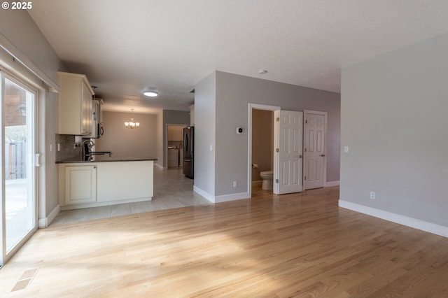 unfurnished living room featuring an inviting chandelier, baseboards, visible vents, and light wood-type flooring