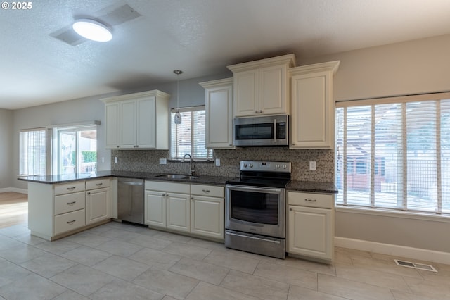 kitchen featuring visible vents, backsplash, appliances with stainless steel finishes, a peninsula, and a sink