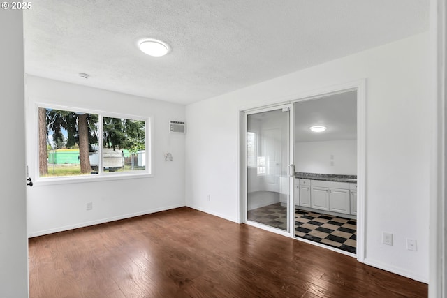 unfurnished bedroom with connected bathroom, a textured ceiling, dark wood finished floors, and baseboards