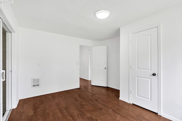 unfurnished bedroom with visible vents, a textured ceiling, dark wood-type flooring, and baseboards