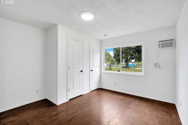 unfurnished bedroom with baseboards, an AC wall unit, dark wood finished floors, and a textured ceiling