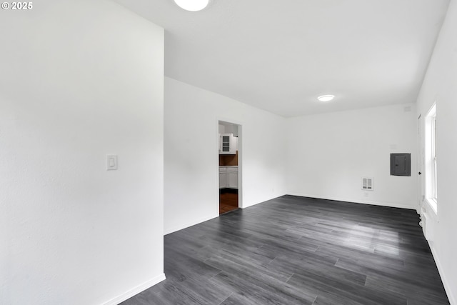 empty room with plenty of natural light, electric panel, visible vents, baseboards, and dark wood-type flooring