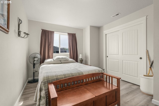 bedroom with baseboards, a closet, light wood finished floors, and visible vents