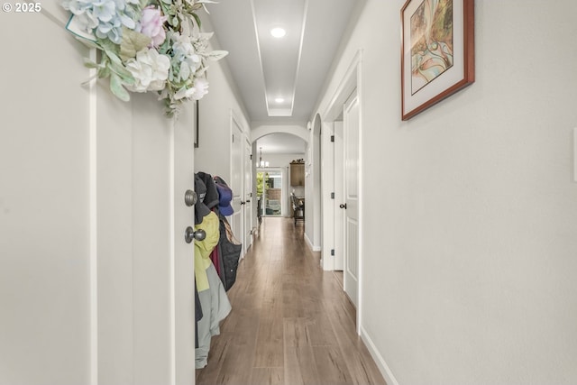 corridor featuring arched walkways, baseboards, recessed lighting, and wood finished floors
