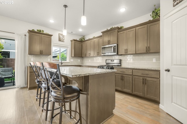kitchen featuring appliances with stainless steel finishes, tasteful backsplash, light wood-style floors, a kitchen bar, and a kitchen island