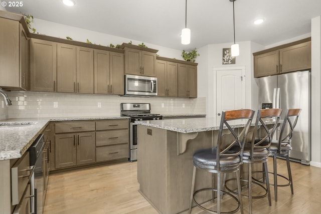 kitchen featuring light stone counters, a sink, a center island, stainless steel appliances, and tasteful backsplash