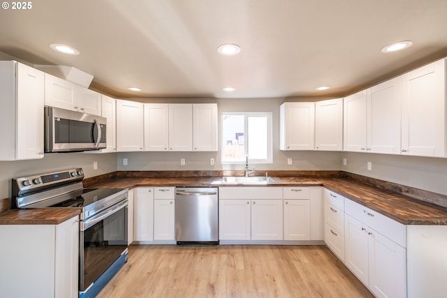 kitchen with white cabinetry, sink, light wood-type flooring, stainless steel appliances, and wood counters