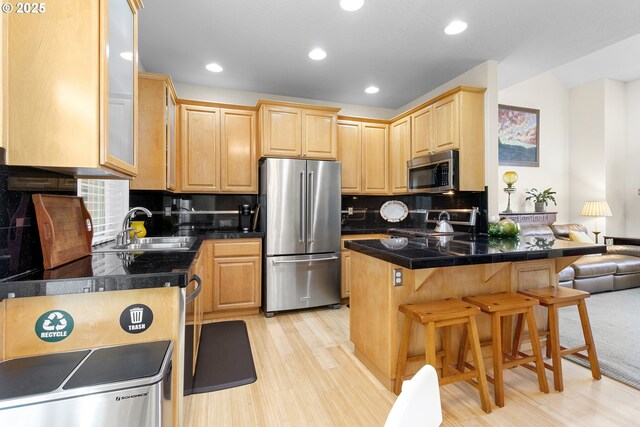 kitchen featuring stainless steel appliances, sink, a breakfast bar area, decorative backsplash, and light brown cabinetry