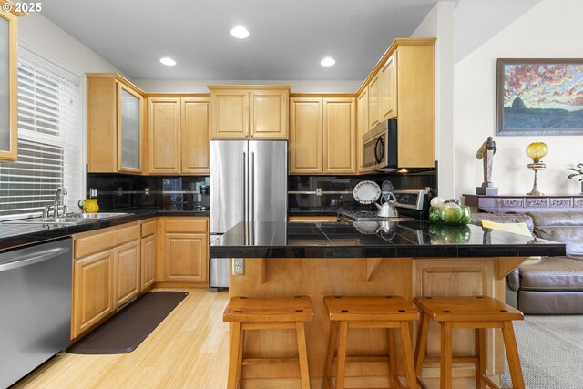 kitchen featuring kitchen peninsula, stainless steel appliances, light brown cabinetry, a kitchen bar, and sink