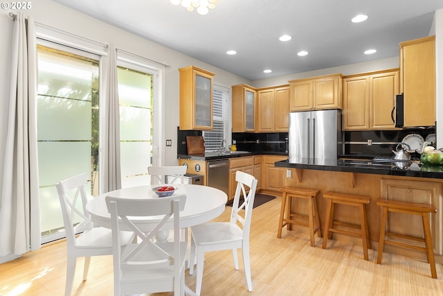 kitchen with appliances with stainless steel finishes, tasteful backsplash, kitchen peninsula, and light wood-type flooring