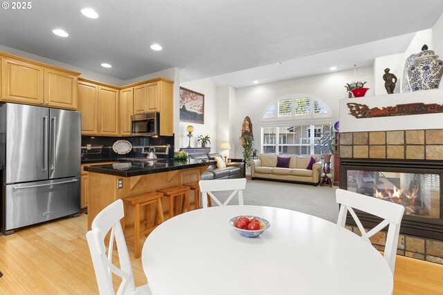 kitchen featuring kitchen peninsula, appliances with stainless steel finishes, a brick fireplace, and light hardwood / wood-style flooring