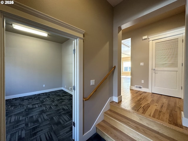 corridor with an upstairs landing, wood finished floors, visible vents, and baseboards