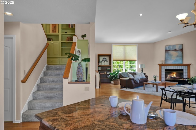 dining space with wood finished floors, stairs, a tile fireplace, a chandelier, and recessed lighting