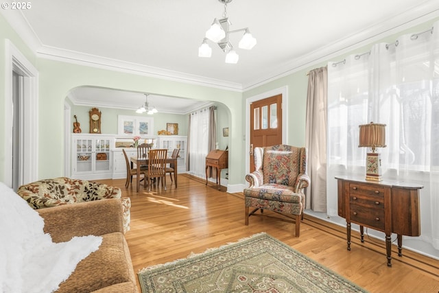 living area with an inviting chandelier, crown molding, arched walkways, and light wood finished floors