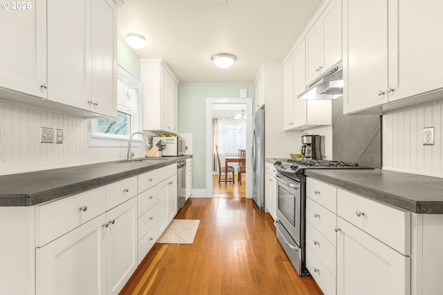 kitchen with dark countertops, under cabinet range hood, white cabinets, stainless steel appliances, and a sink