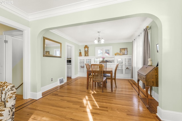 dining area with arched walkways, visible vents, light wood-style flooring, and crown molding