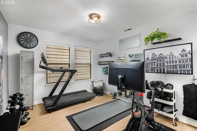 workout room featuring baseboards, wood finished floors, visible vents, and a textured ceiling