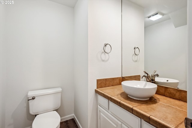 bathroom with vanity, toilet, wood finished floors, and baseboards