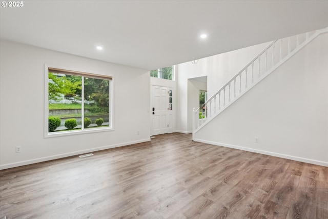 unfurnished living room with healthy amount of natural light, wood finished floors, stairway, baseboards, and recessed lighting