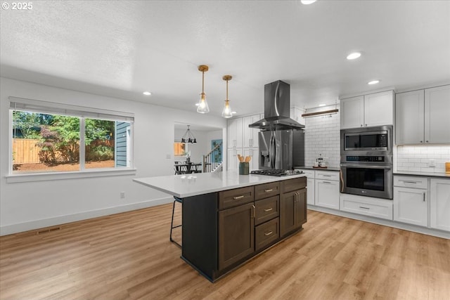 4992 Prospect St, West Linn, OR 97068 - kitchen featuring stainless steel appliances, island exhaust hood, backsplash, light wood-style flooring, and a breakfast bar area