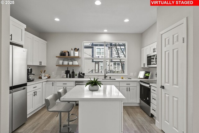 kitchen featuring a kitchen island, light countertops, a sink, light wood-style flooring, and appliances with stainless steel finishes