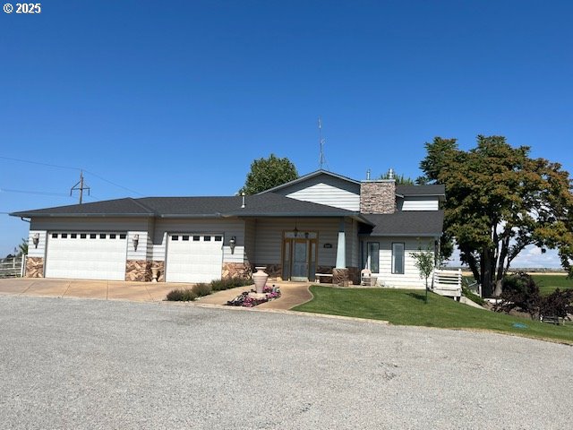 view of front of house featuring a chimney, an attached garage, stone siding, driveway, and a front lawn