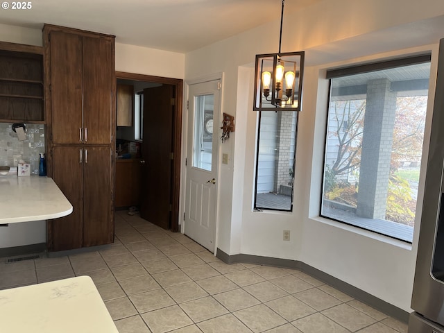 unfurnished dining area featuring light tile patterned flooring, baseboards, and an inviting chandelier