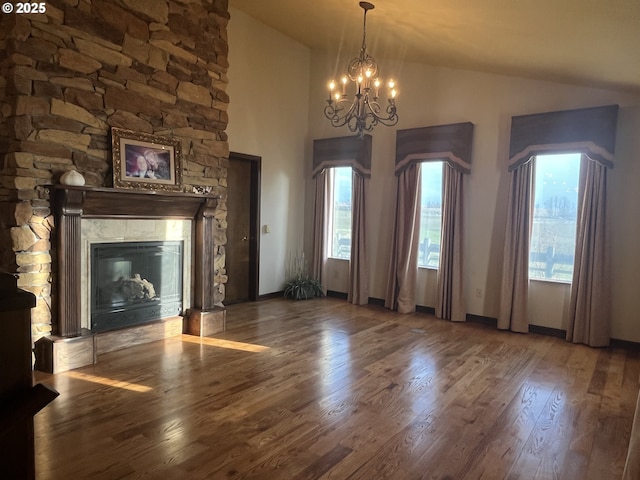 unfurnished living room featuring baseboards, wood finished floors, vaulted ceiling, a stone fireplace, and a notable chandelier