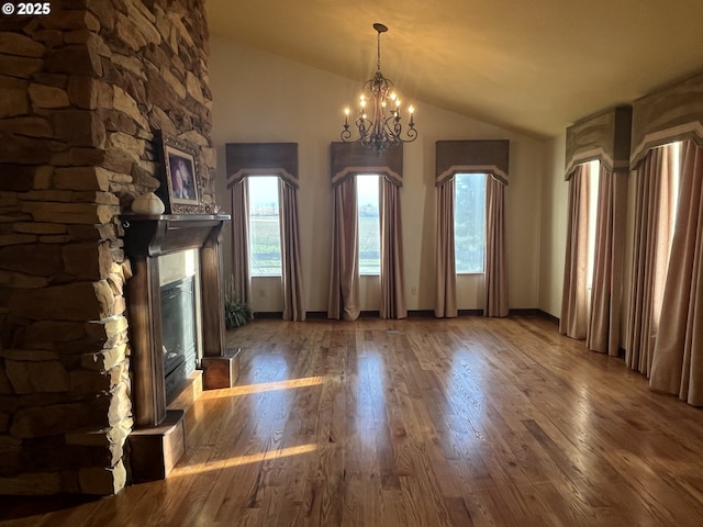 unfurnished living room featuring baseboards, wood finished floors, vaulted ceiling, a stone fireplace, and a chandelier