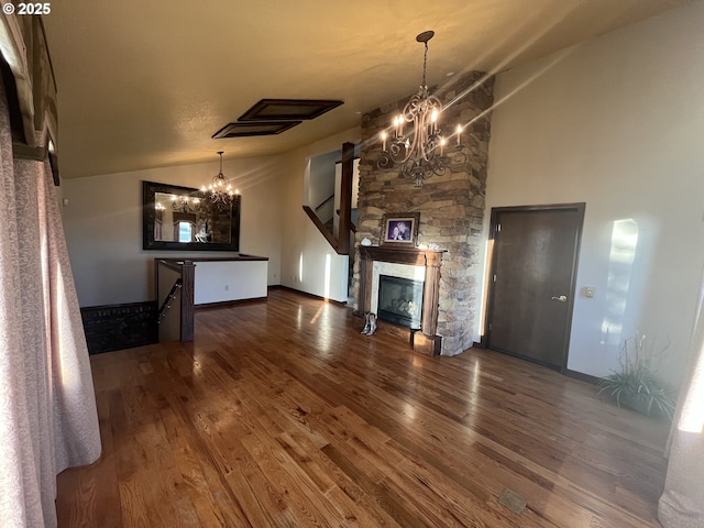 unfurnished living room featuring an inviting chandelier, vaulted ceiling, wood finished floors, and a stone fireplace