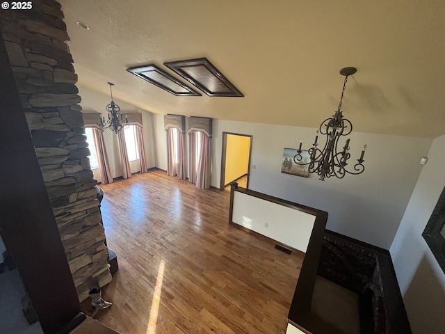 interior space with a notable chandelier, baseboards, visible vents, lofted ceiling, and wood finished floors