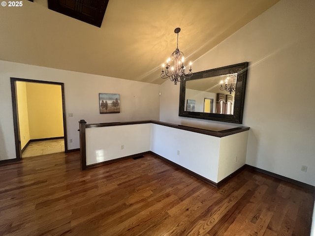 empty room featuring baseboards, wood finished floors, a notable chandelier, and lofted ceiling